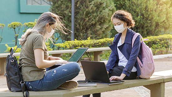 two students sitting outside wearing PPE/facemasks