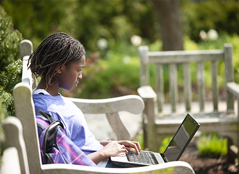 female student working on a laptop outside in the summer