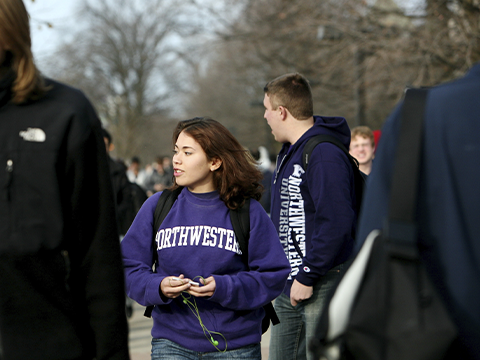 female student wearing Northwestern sweatshirt walking on campus among other students