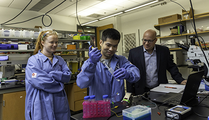 two students working with a professor in a lab